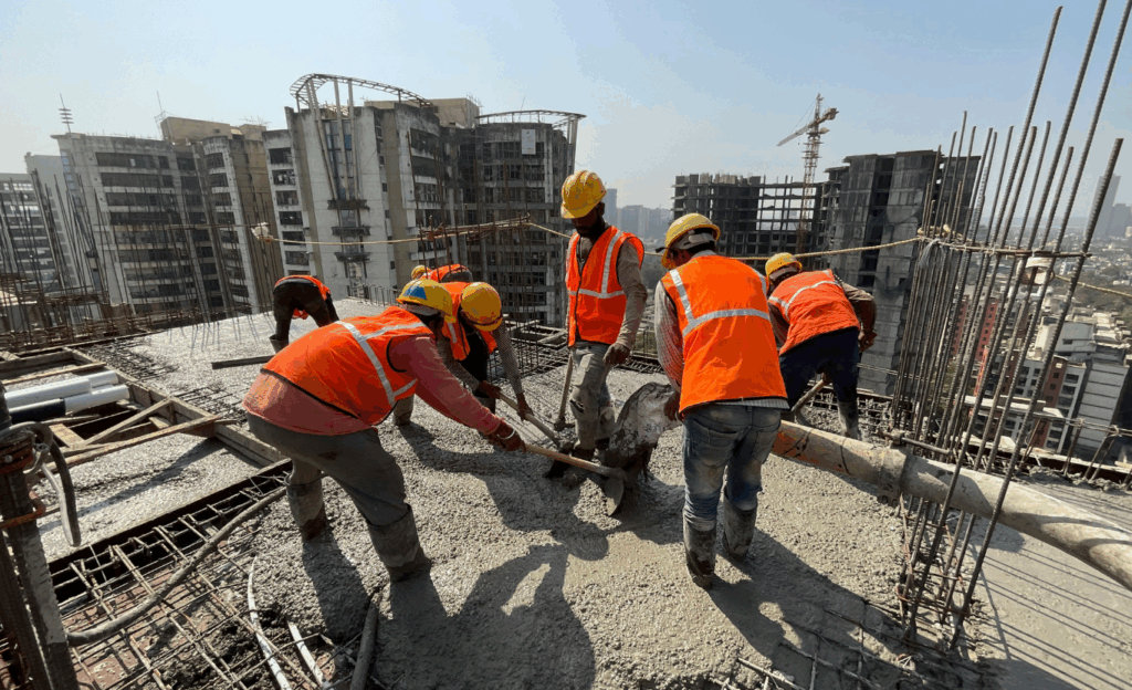 Operários concretando laje em obra de prédio com EPIs e protocolo de segurança.
