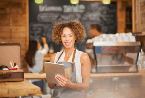 Mulher empreendedora em cafeteria usando tablet, representando a importância de um canal de denúncias para pequenas e médias empresas.