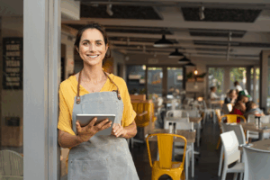 Mulher empreendedora em restaurante sorrindo, segurando um tablet. A imagem destaca a gestão moderna de negócios, com foco no uso de tecnologia para facilitar processos, como a implementação de um canal de denúncias em PME.