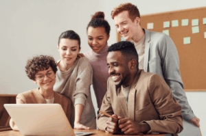 Grupo diverso de profissionais reunidos em frente a um laptop, demonstrando cooperação e engajamento