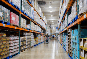 Corredor de um grande centro de distribuição com produtos empilhados em paletes, ilustrando a importância do Canal de denúncias no varejo e atacado para garantir transparência e ética nas operações.