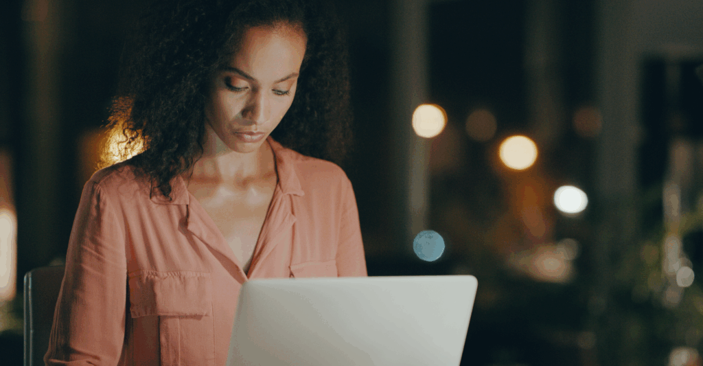 Mulher trabalhando em um laptop à noite enquanto analisa dados, simbolizando Boas práticas ISO 37002:2021 em canal de denúncias.