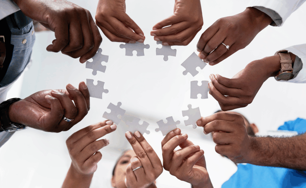 Múltiplas mãos segurando peças de quebra-cabeça formando um círculo, simbolizando união e Boas práticas ISO 37002:2021 em canal de denúncias.