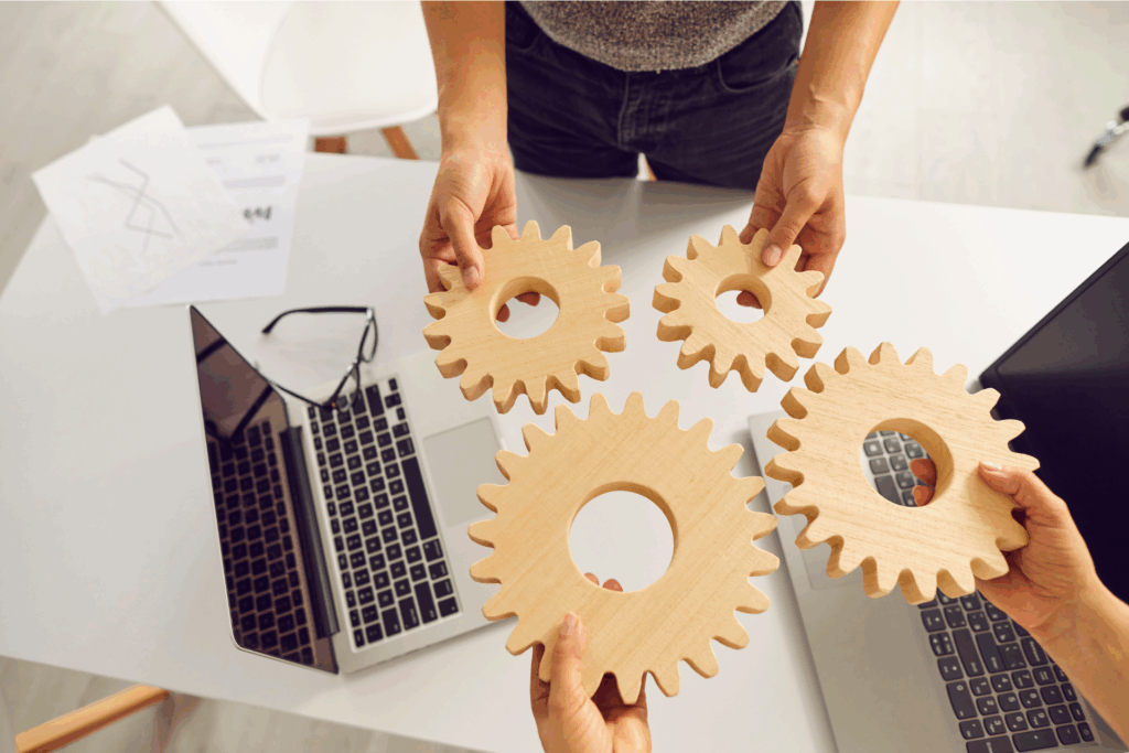 Pessoas segurando engrenagens de madeira sobre uma mesa de trabalho, simbolizando colaboração, governança e o papel do canal de denúncias em cooperativas na integração de processos éticos.