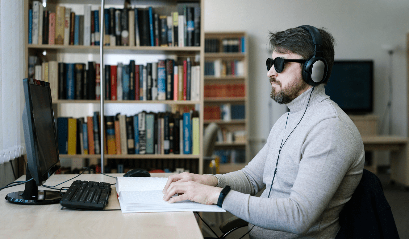 Homem com deficiência visual usando computador e fones de ouvido, demonstrando autonomia e canal de denúncias acessível ABNT NBR 17225