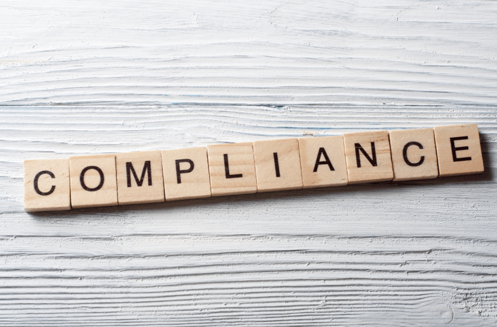 Palavra compliance formada por blocos de madeira representando canal de denúncias riscos psicossociais NR-1 e conformidade empresarial.