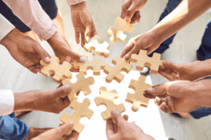 Equipe unindo peças de quebra-cabeça em uma dinâmica colaborativa que representa a construção de uma cultura ética baseada em código de conduta política anti-assédio canal de denúncias CIPAA, promovendo respeito, inclusão e cooperação no ambiente de trabalho.
